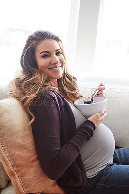 Buy stock photo Cropped portrait of an attractive young pregnant woman eating breakfast while sitting on the sofa at home