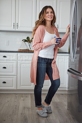 Buy stock photo Shot of a beautiful young woman having coffee while standing by the refrigerator in the kitchen at home