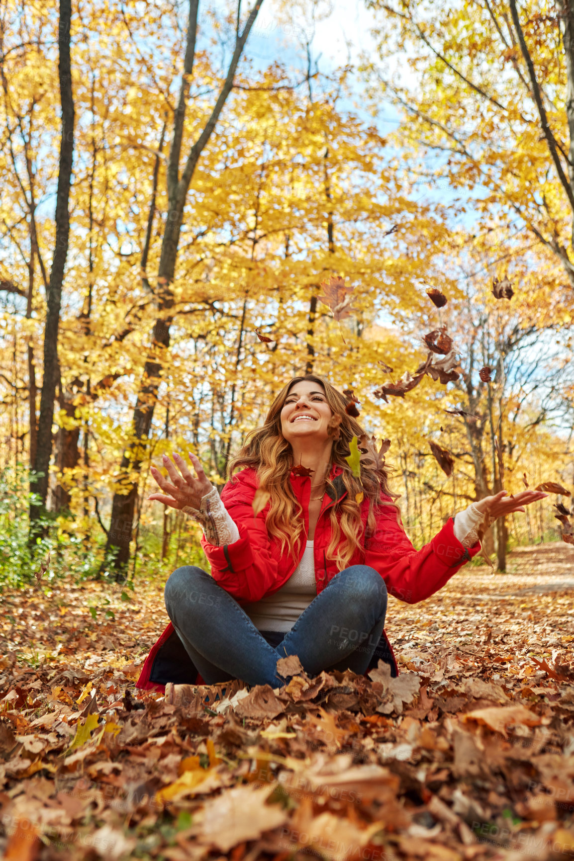 Buy stock photo Full length shot of an attractive young woman throwing leaves while sitting in the forest during autumn