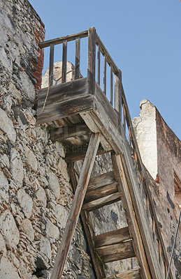 Buy stock photo Old wooden stairs leading up to a rooftop of a historic building against a blue sky background. Weathered staircase    and a vintage stone wall background. Spot to watch the view and get fresh air