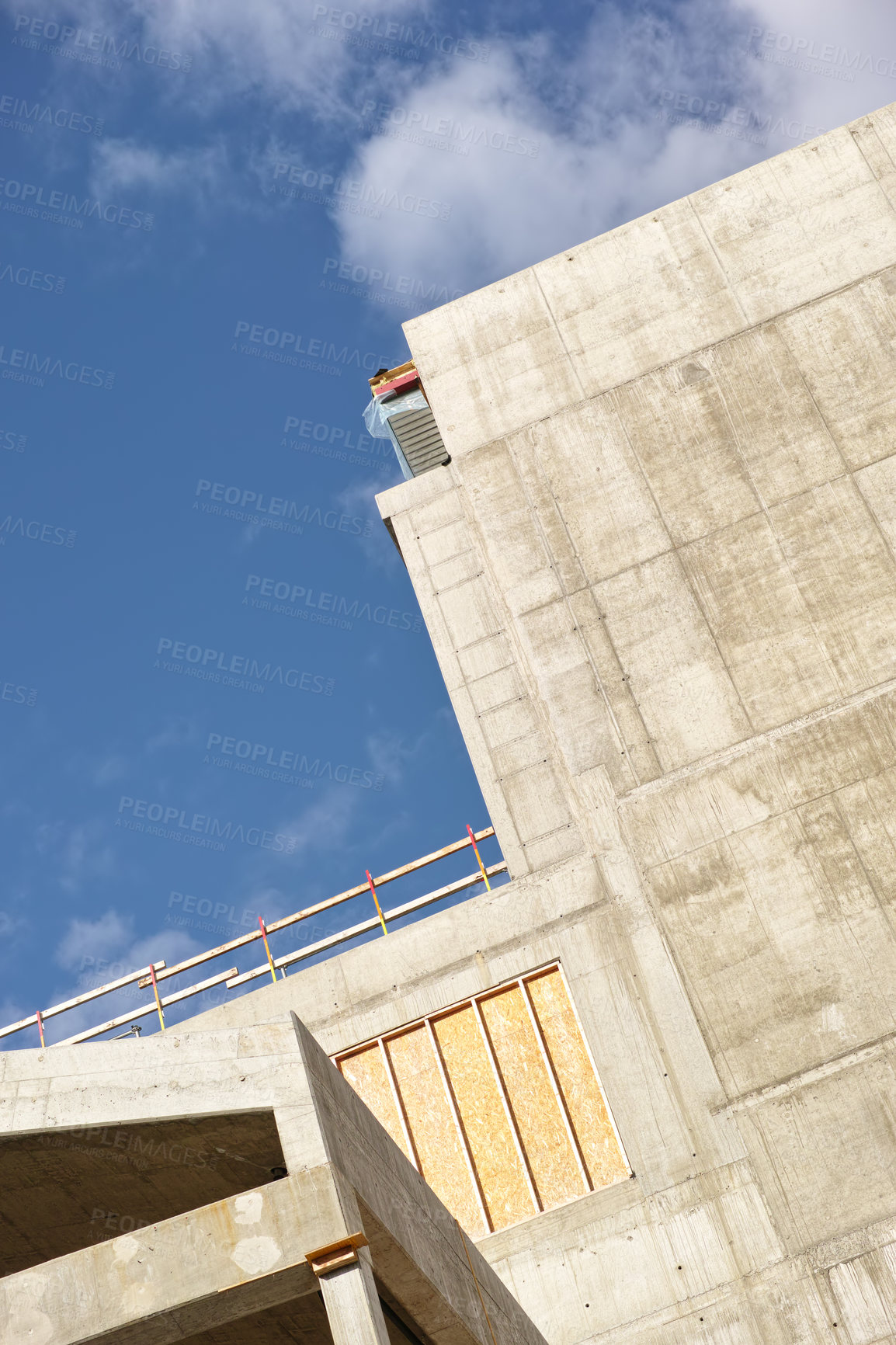 Buy stock photo Exterior of a concrete building against a cloudy blue sky. Detail view of a tall residential or office building made of exposed concrete slabs. Construction phase of home remodel and addition