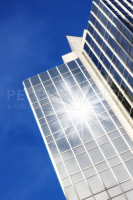 Buy stock photo Geometric glass windows on a skyscraper with sun reflecting a lens flare against a blue sky background from below. Exterior architectural details of a modern and tall high rise building in the city