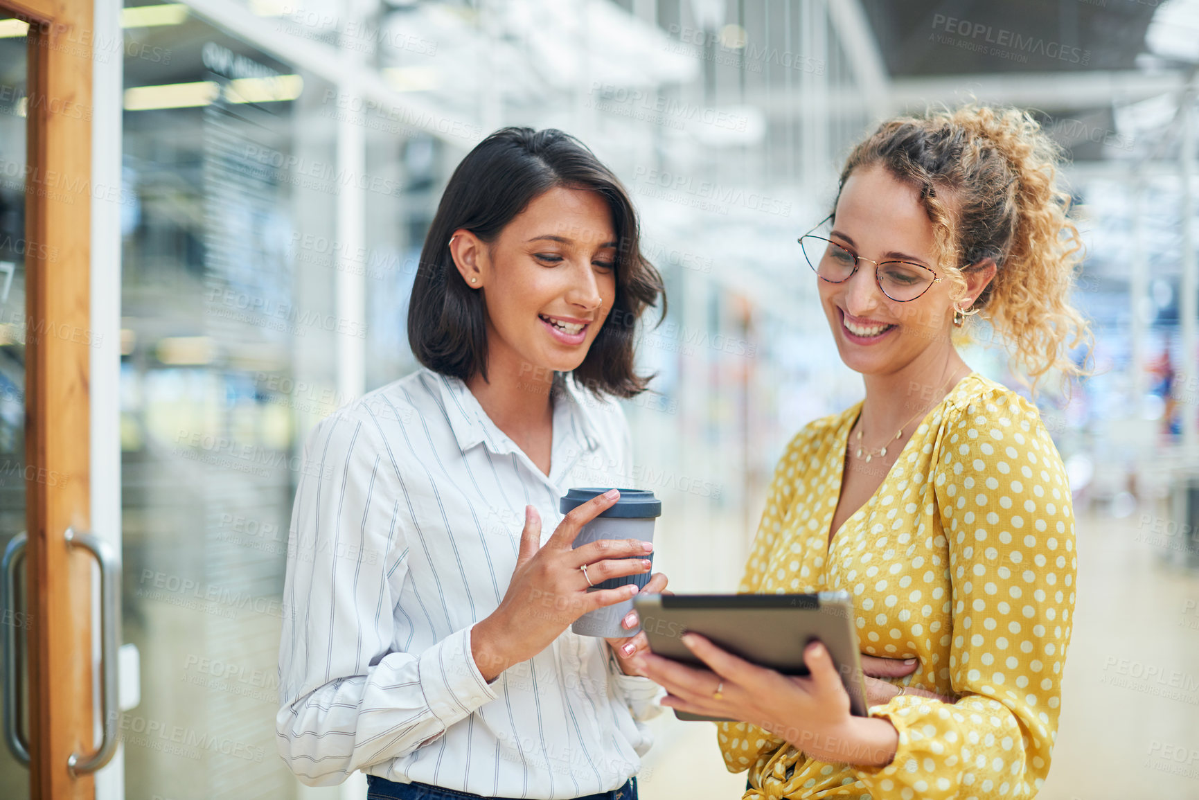 Buy stock photo Shot of two young businesswomen using a digital tablet in a modern office