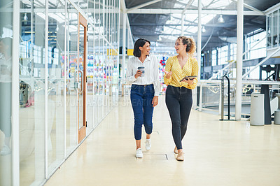 Buy stock photo Shot of two young businesswomen having a discussion while walking through a modern office