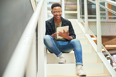 Buy stock photo Shot of a young businessman using a digital tablet on the stairs of a modern office