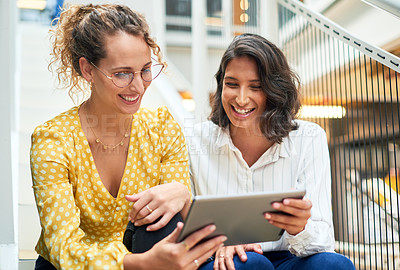 Buy stock photo Shot of two young businesswomen using a digital tablet in a modern office