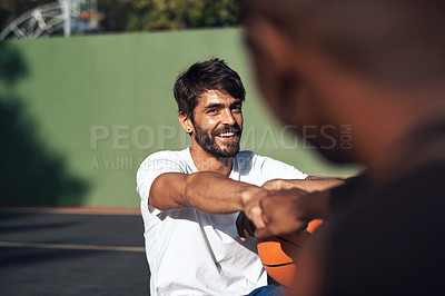 Buy stock photo Shot of a sporty young man giving his teammate a fist bump on a basketball court