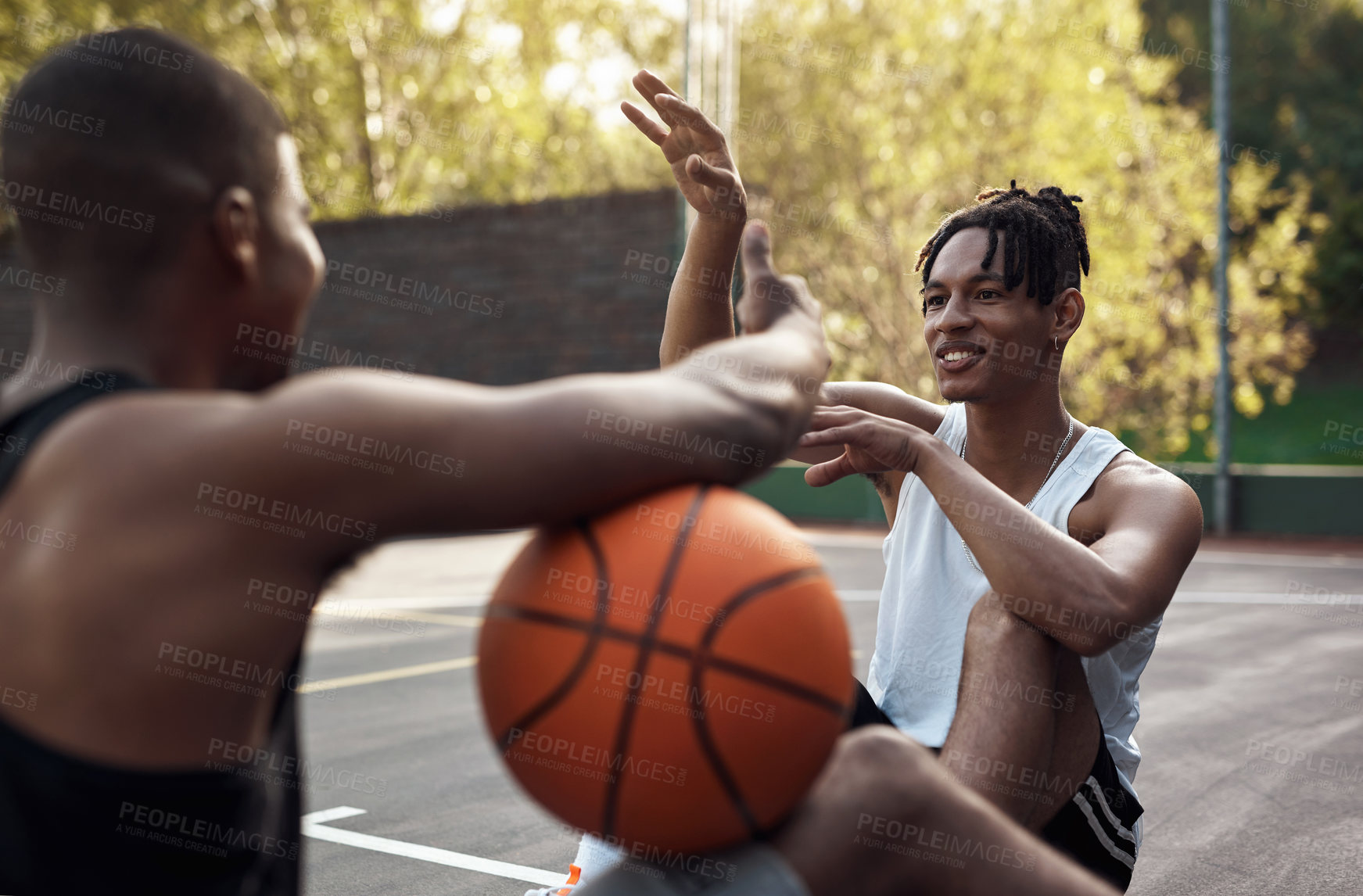 Buy stock photo Shot of two sporty young men chatting to each other on a basketball court