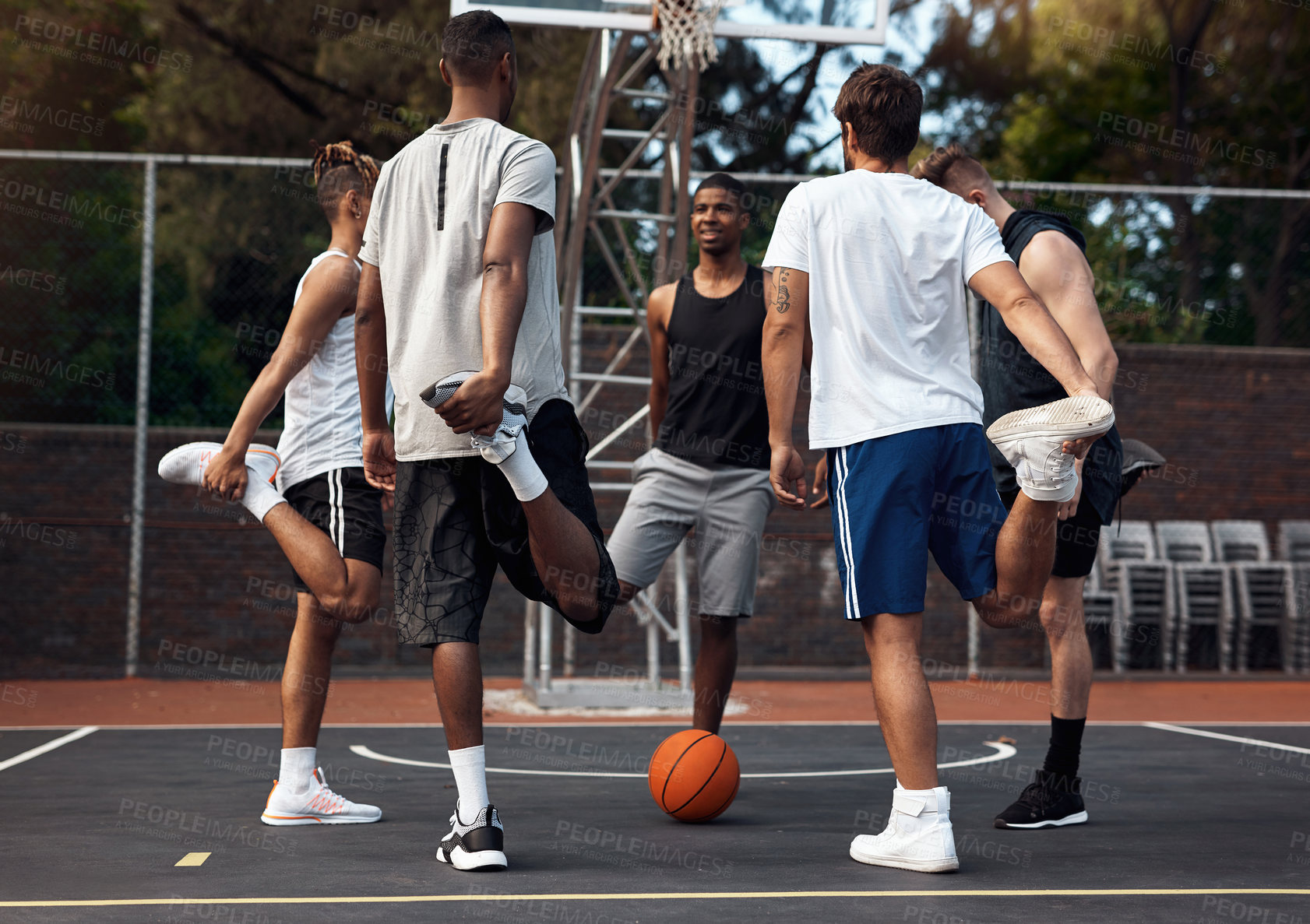 Buy stock photo Shot of a group of sporty young men stretching their legs on a basketball court