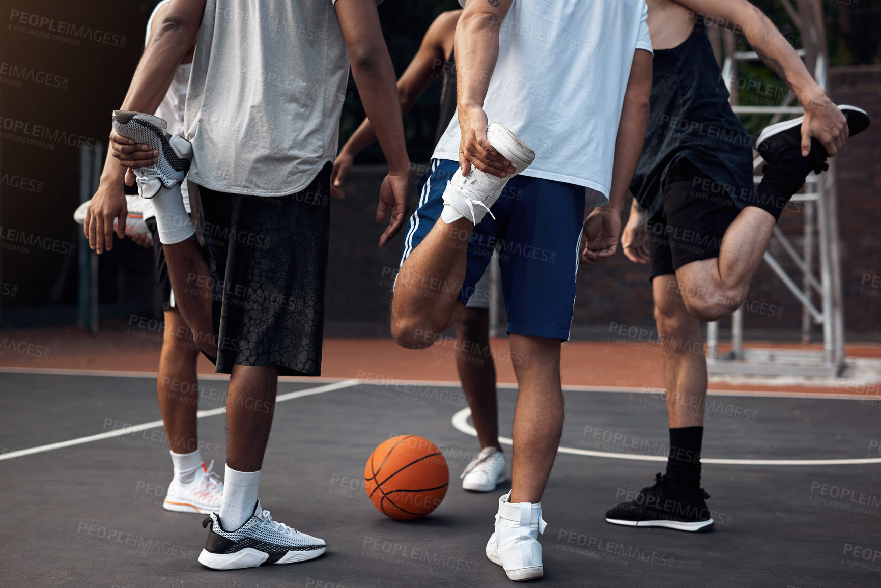 Buy stock photo Closeup shot of a group of sporty young men stretching their legs on a basketball court