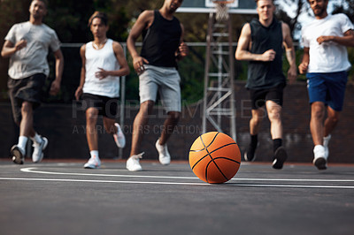 Buy stock photo Closeup shot of a basketball on a sports court with a group of young men in the background
