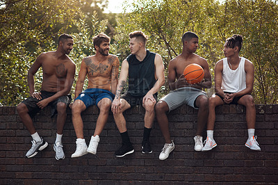 Buy stock photo Shot of a group of sporty young men sitting on a wall after a game of basketball