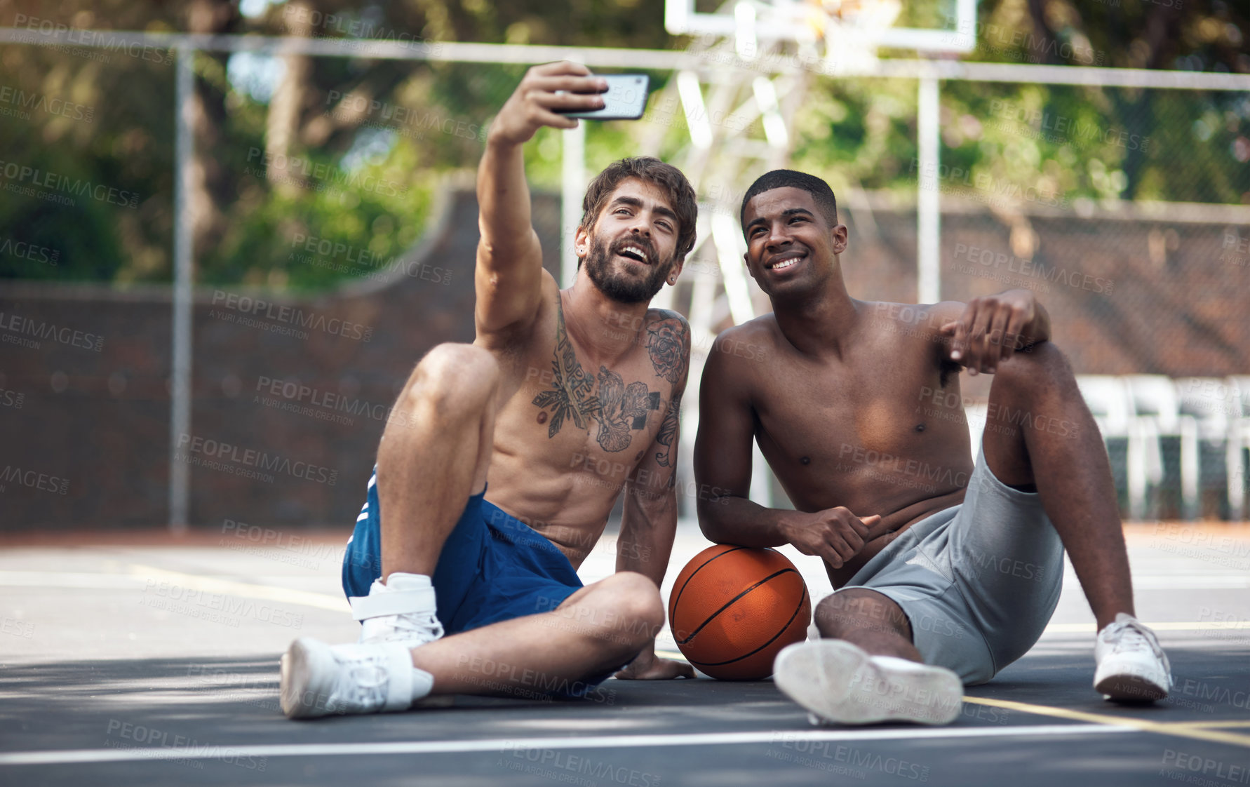 Buy stock photo Shot of two sporty young men taking selfies on a basketball court