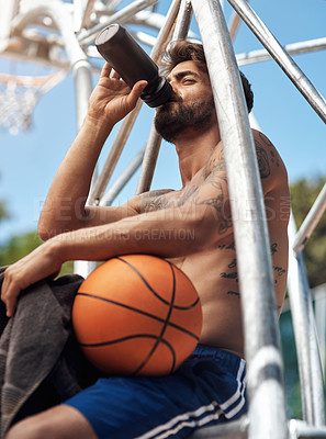 Buy stock photo Shot of a sporty young man drinking water while taking a break on a sports court