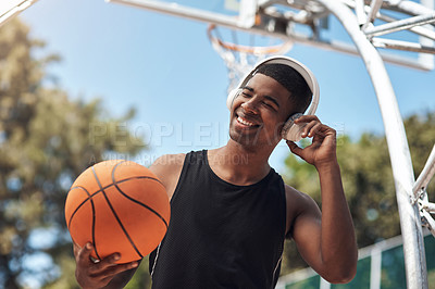 Buy stock photo Shot of a sporty young man listening to music while playing basketball on a sports court