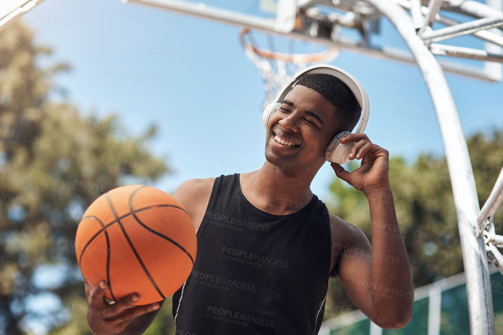 Buy stock photo Shot of a sporty young man listening to music while playing basketball on a sports court