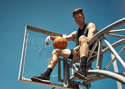 Buy stock photo Portrait of a sporty young man sitting on a basketball hoop on a sports court