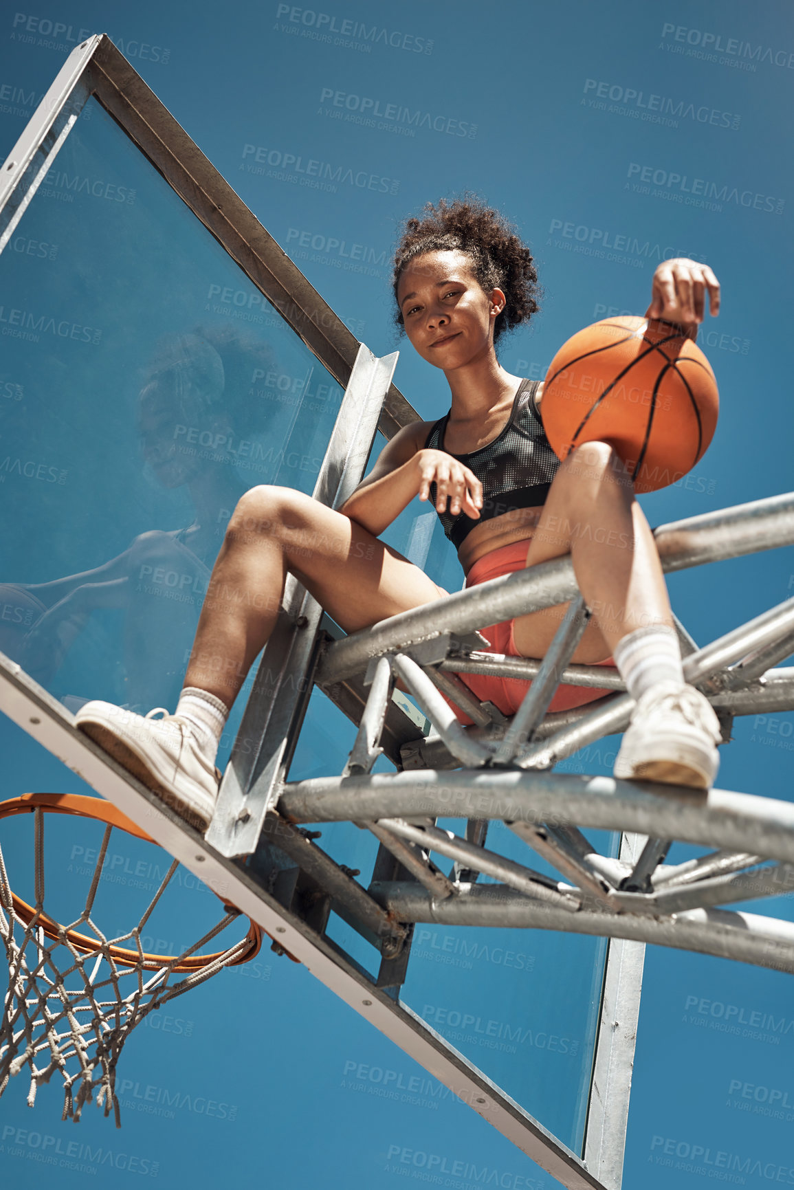 Buy stock photo Portrait of a sporty young woman sitting on a basketball hoop on a sports court