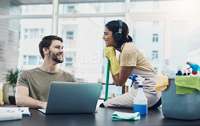 Buy stock photo Shot of a young woman cleaning the house while her husband uses a laptop