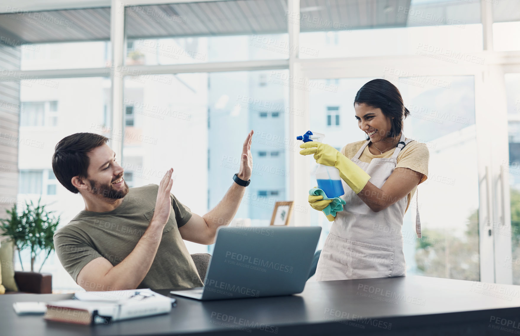 Buy stock photo Shot of a young woman having fun with her husband while she cleans the house and he uses a laptop