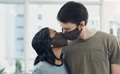 Buy stock photo Shot of a young couple kissing each other while wearing masks at home