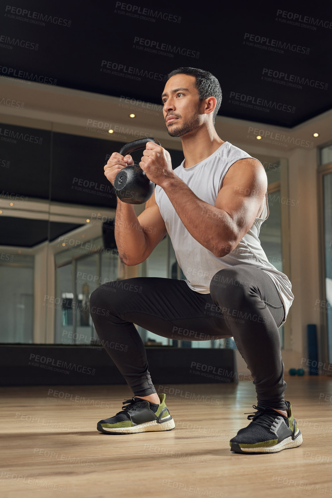Buy stock photo Full length shot of a handsome young male athlete doing squats while holding a kettle bell in the gym