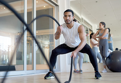 Buy stock photo Shot of a man using battle ropes while working out at the gym