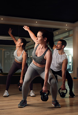 Buy stock photo Full length shot of three young athletes working out with kettle bells in the gym
