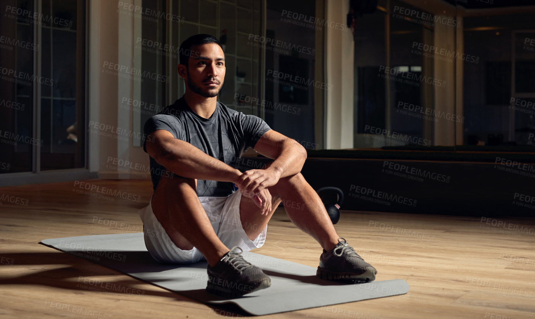 Buy stock photo Full length shot of a handsome young male athlete sitting on an exercise mat in the gym