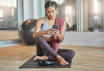Buy stock photo Full length shot of an attractive young female athlete checking her phone while sitting in the gym