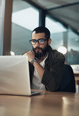 Buy stock photo Shot of a young businessman using a laptop during a late night in a modern office