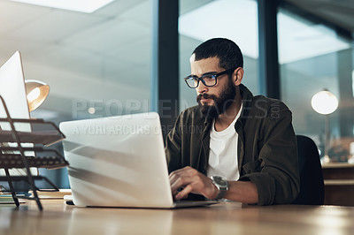 Buy stock photo Shot of a young businessman using a laptop during a late night in a modern office