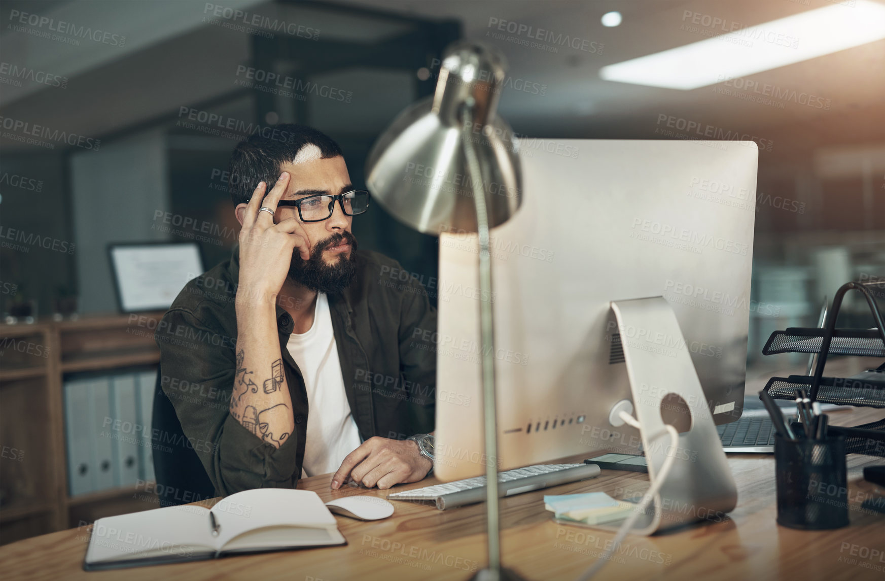 Buy stock photo Shot of a young businessman using a computer during a late night in a modern office