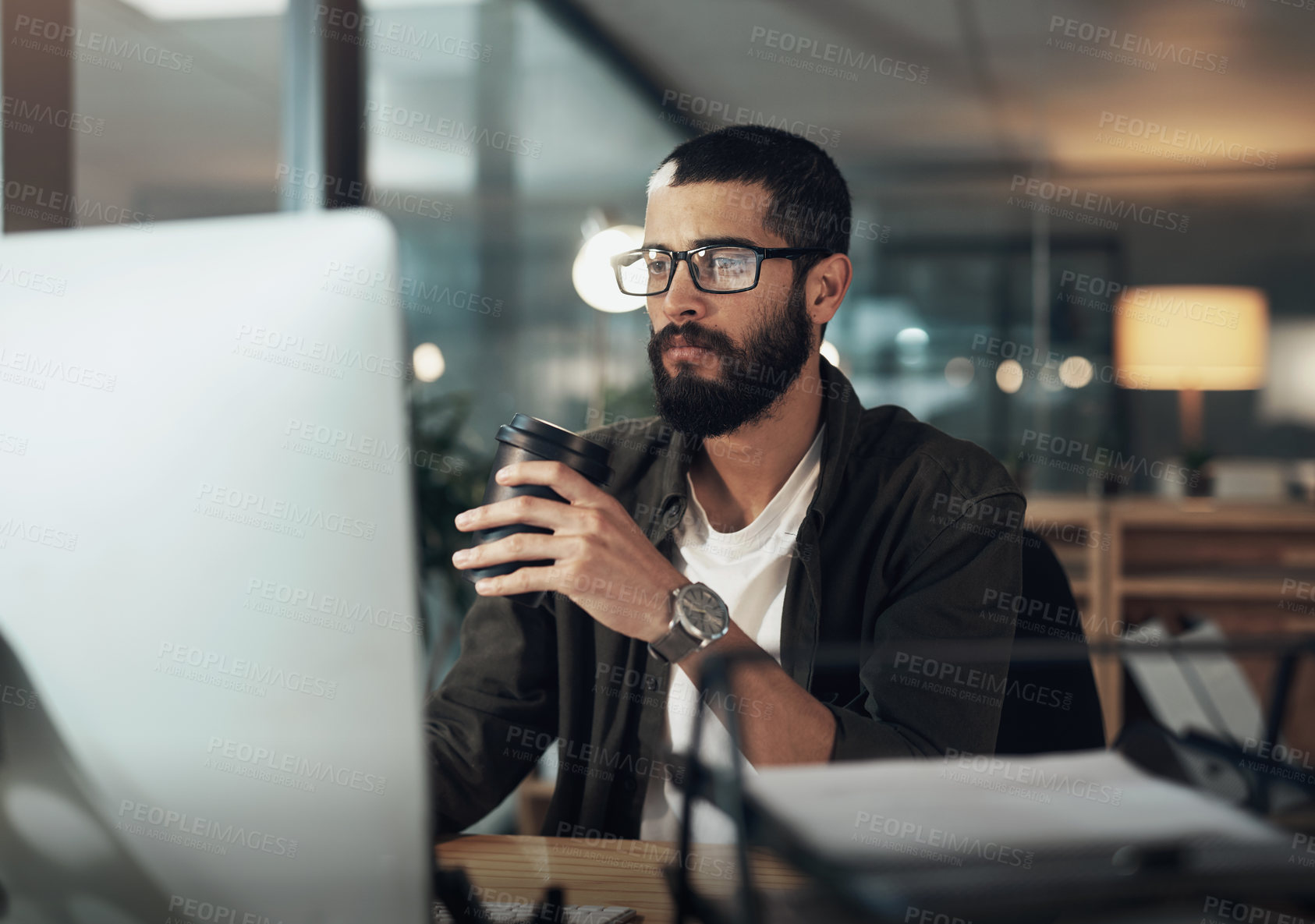 Buy stock photo Shot of a young businessman having coffee and using a computer during a late night in a modern office