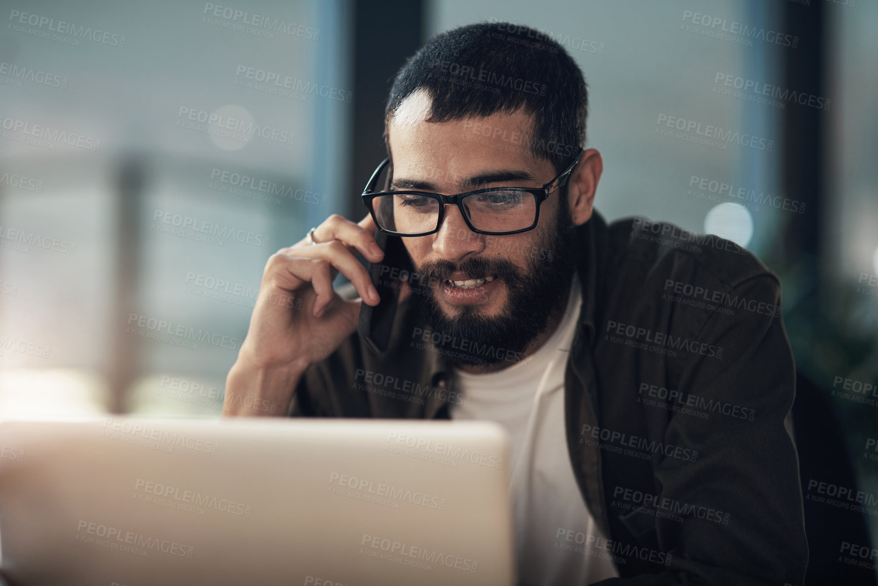 Buy stock photo Shot of a young businessman using a laptop and smartphone during a late night in a modern office