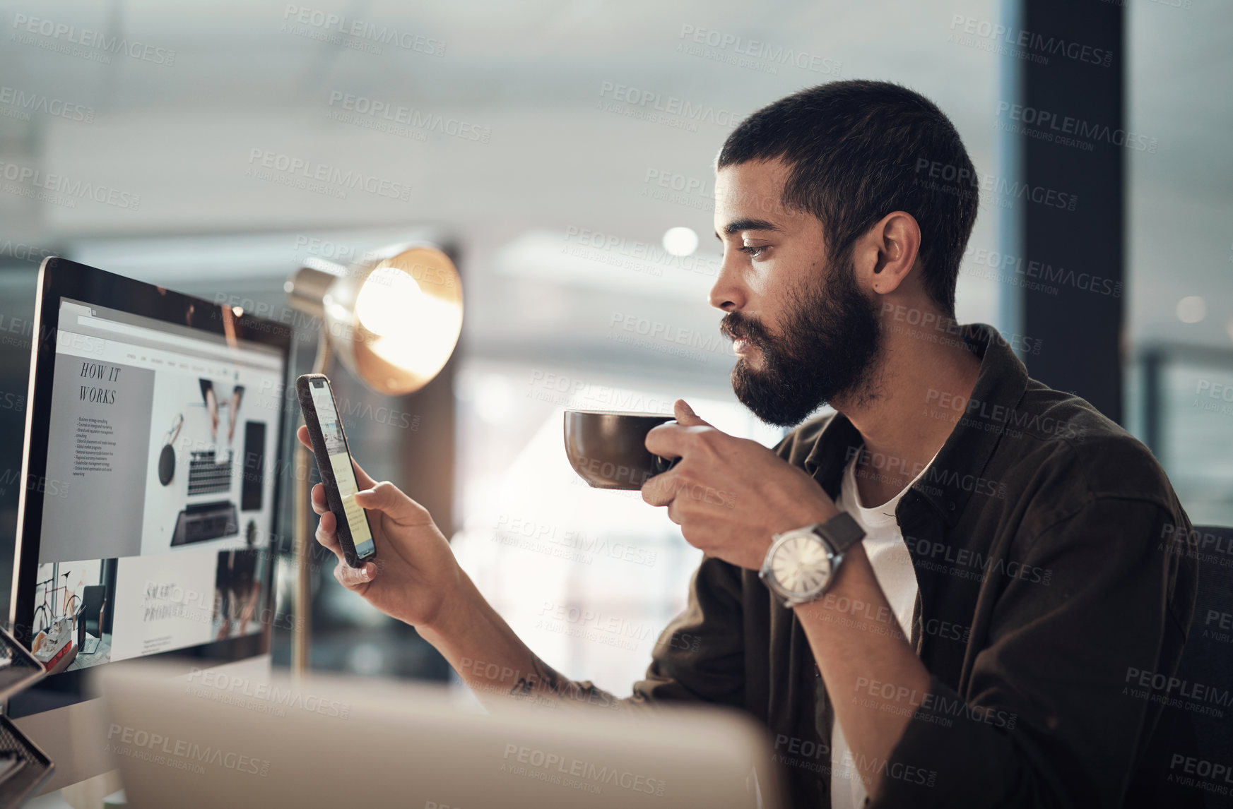 Buy stock photo Shot of a young businessman having coffee and using a smartphone during a late night in a modern office