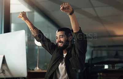 Buy stock photo Shot of a young businessman cheering while using a computer during a late night at work