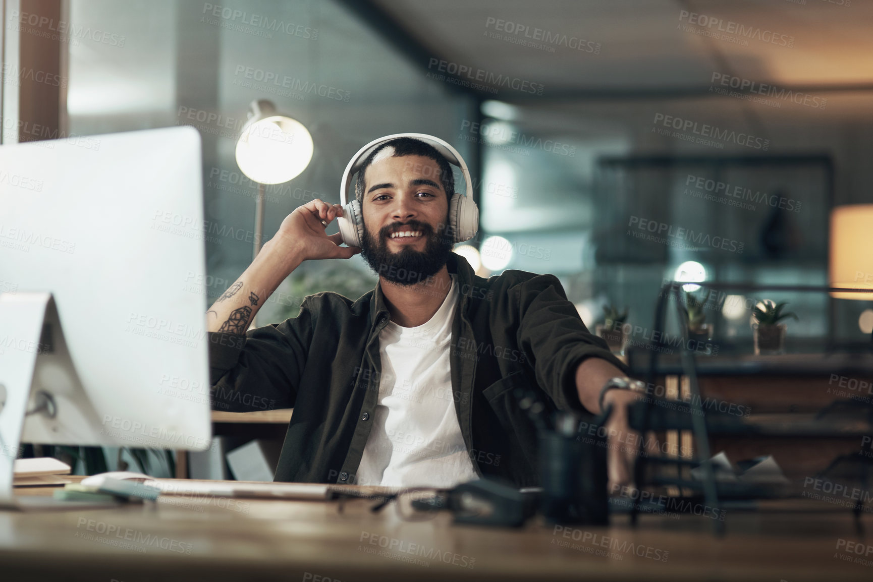 Buy stock photo Shot of a young businessman using a computer and headphones during a late night at work