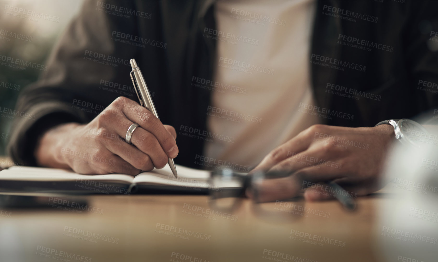 Buy stock photo Shot of an unrecognisable businessman writing in a notebook during a late night at work