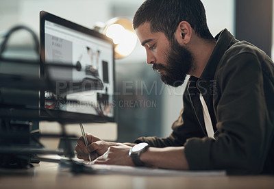 Buy stock photo Shot of a young businessman writing in a notebook and using a computer during a late night at work