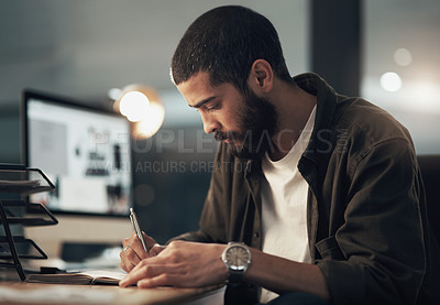 Buy stock photo Shot of a young businessman writing in a notebook during a late night at work