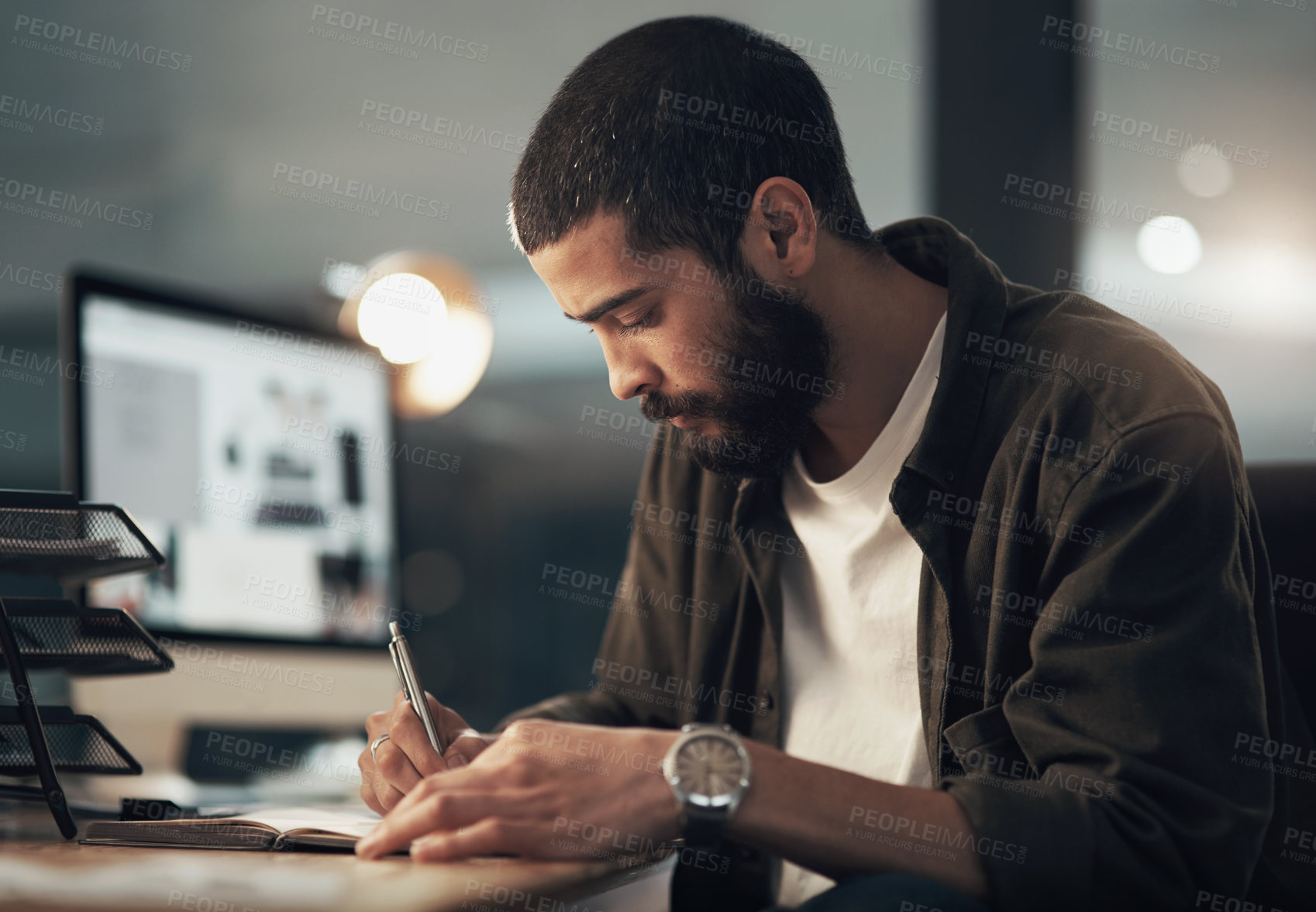 Buy stock photo Shot of a young businessman writing in a notebook during a late night at work