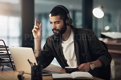 Buy stock photo Shot of a young businessman using a laptop and headphones during a late night at work