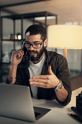Buy stock photo Shot of a young businessman using a smartphone and laptop during a late night at work