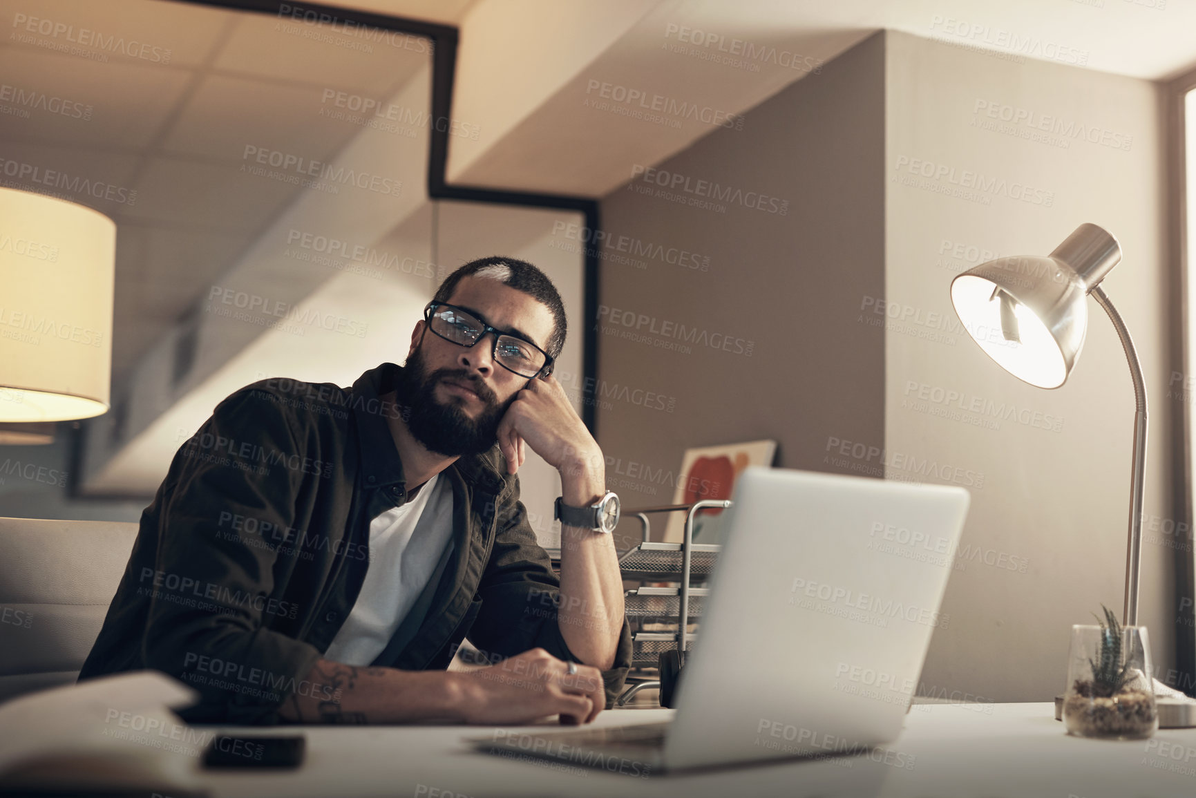 Buy stock photo Shot of a young businessman looking uncertain while working late at night in a modern office
