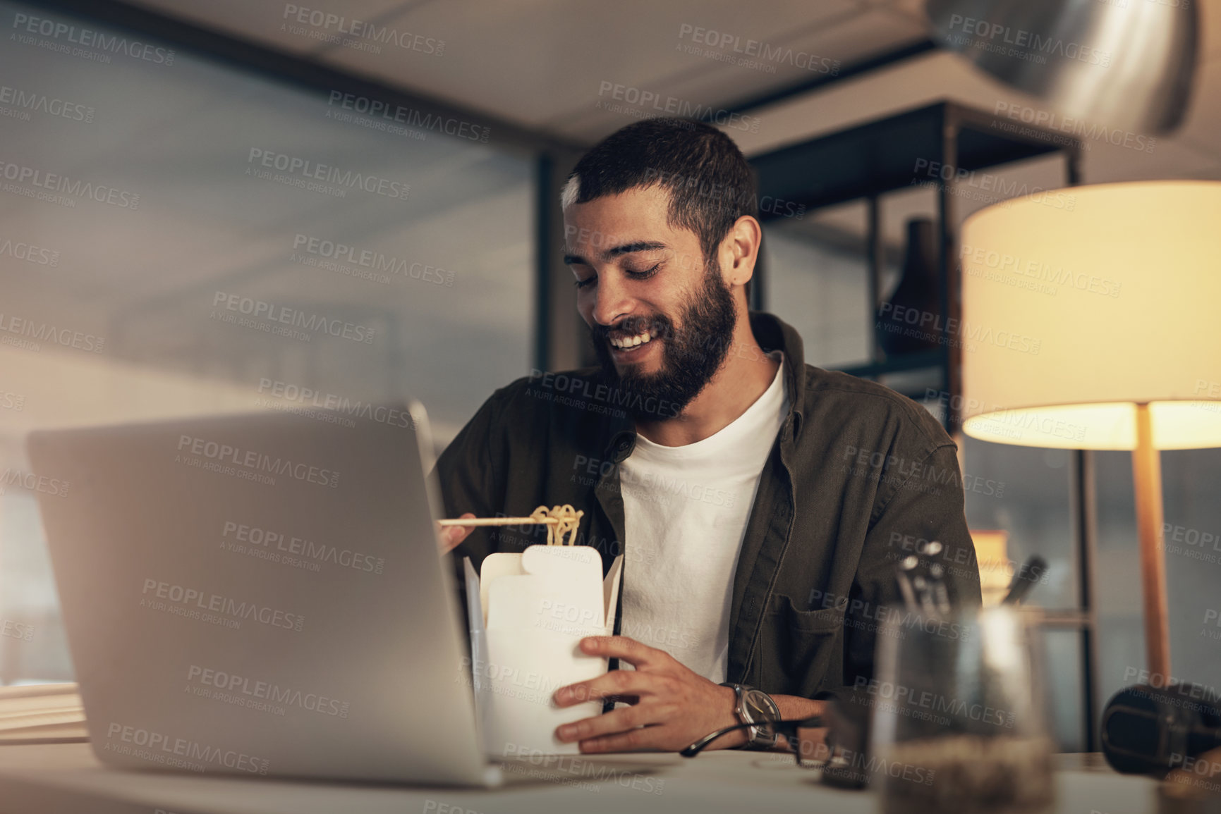 Buy stock photo Shot of a young businessman having takeout and using a laptop during a late night at work