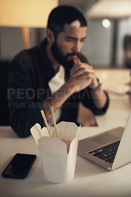 Buy stock photo Shot of a young businessman having takeout and using a laptop during a late night at work