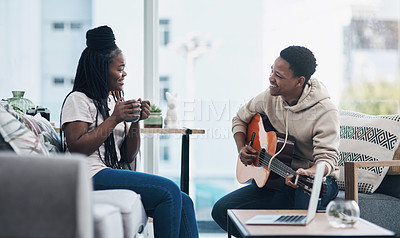 Buy stock photo Shot of a young man playing the guitar while his wife has a cup of coffee at home