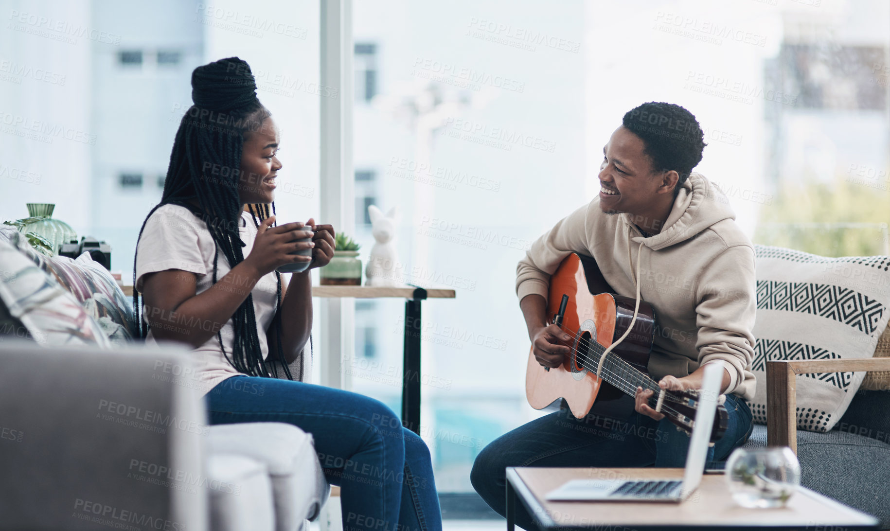 Buy stock photo Shot of a young man playing the guitar while his wife has a cup of coffee at home