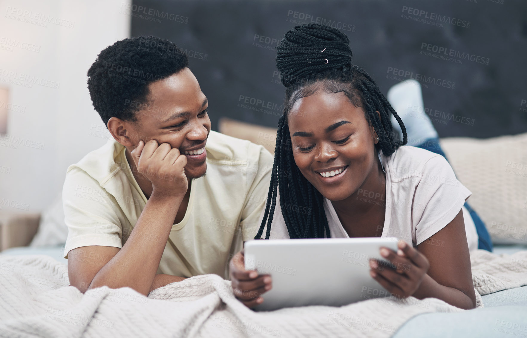 Buy stock photo Shot of a young couple using a digital tablet while relaxing on their bed at home